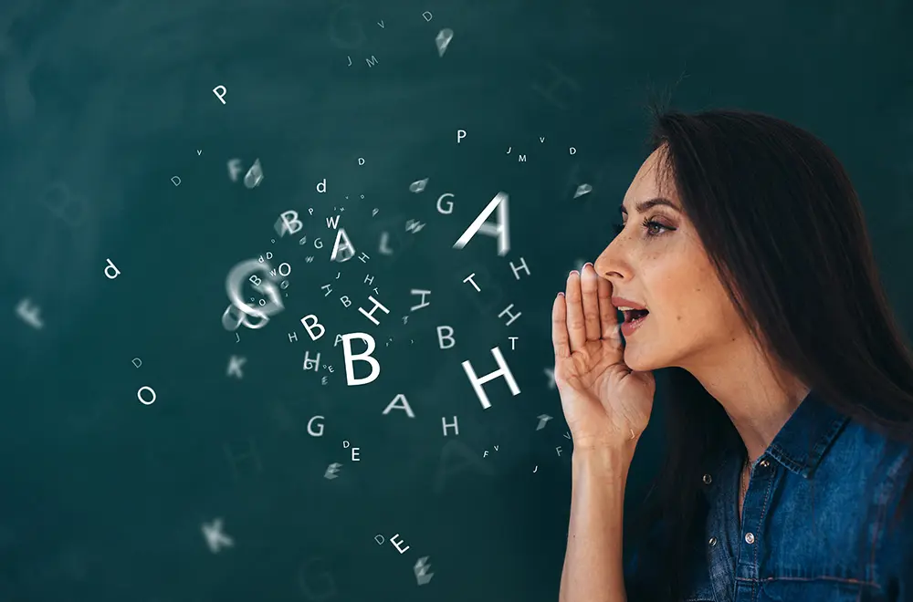 A woman stands in front of a chalkboard, holding her hand near her mouth as she speaks. Floating letters emerge from her mouth, symbolizing speech, communication, or language.